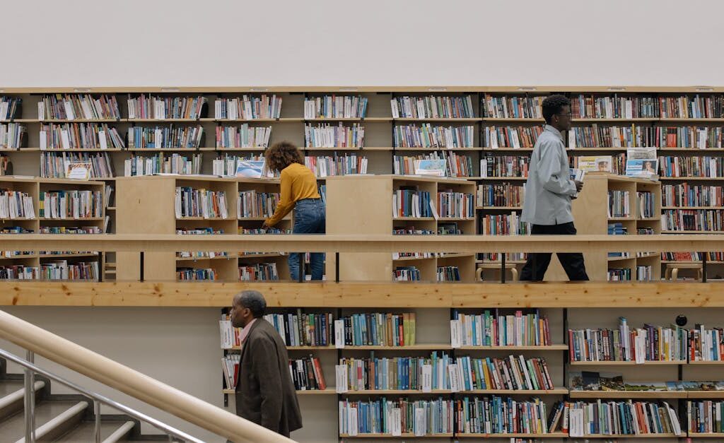 Three adults browsing books in a modern public library filled with shelves and staircases.